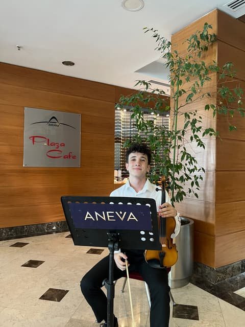 Aneva kemancısı, otel lobisinde Aneva nota sehpasının başında keman çalıyor