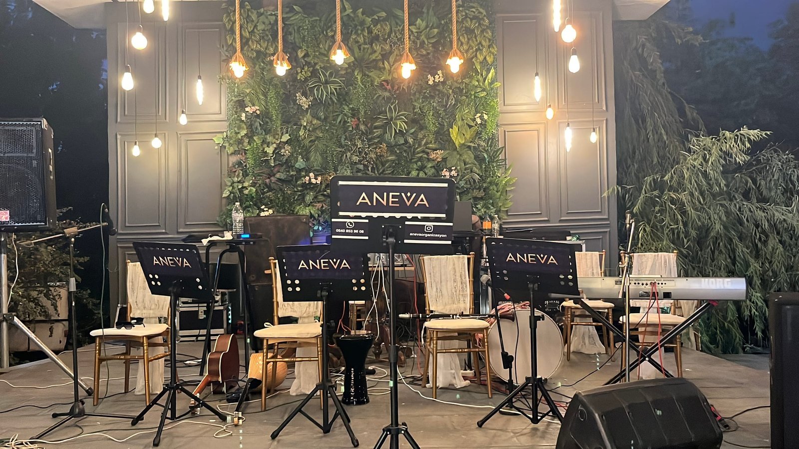 Aneva nota sehpalarıyla hazırlanmış orkestra sahnesi; yeşil duvar ve sarkıt aydınlatma